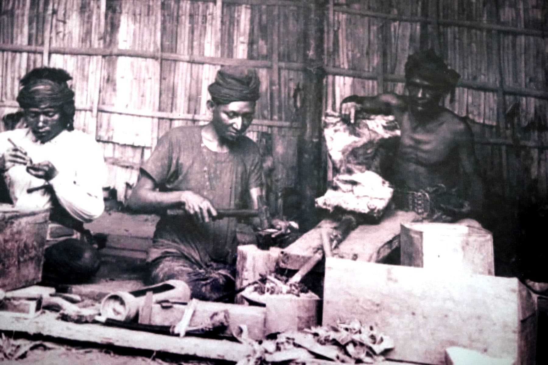 Archival photograph of three artisans working inside a bamboo-walled workshop