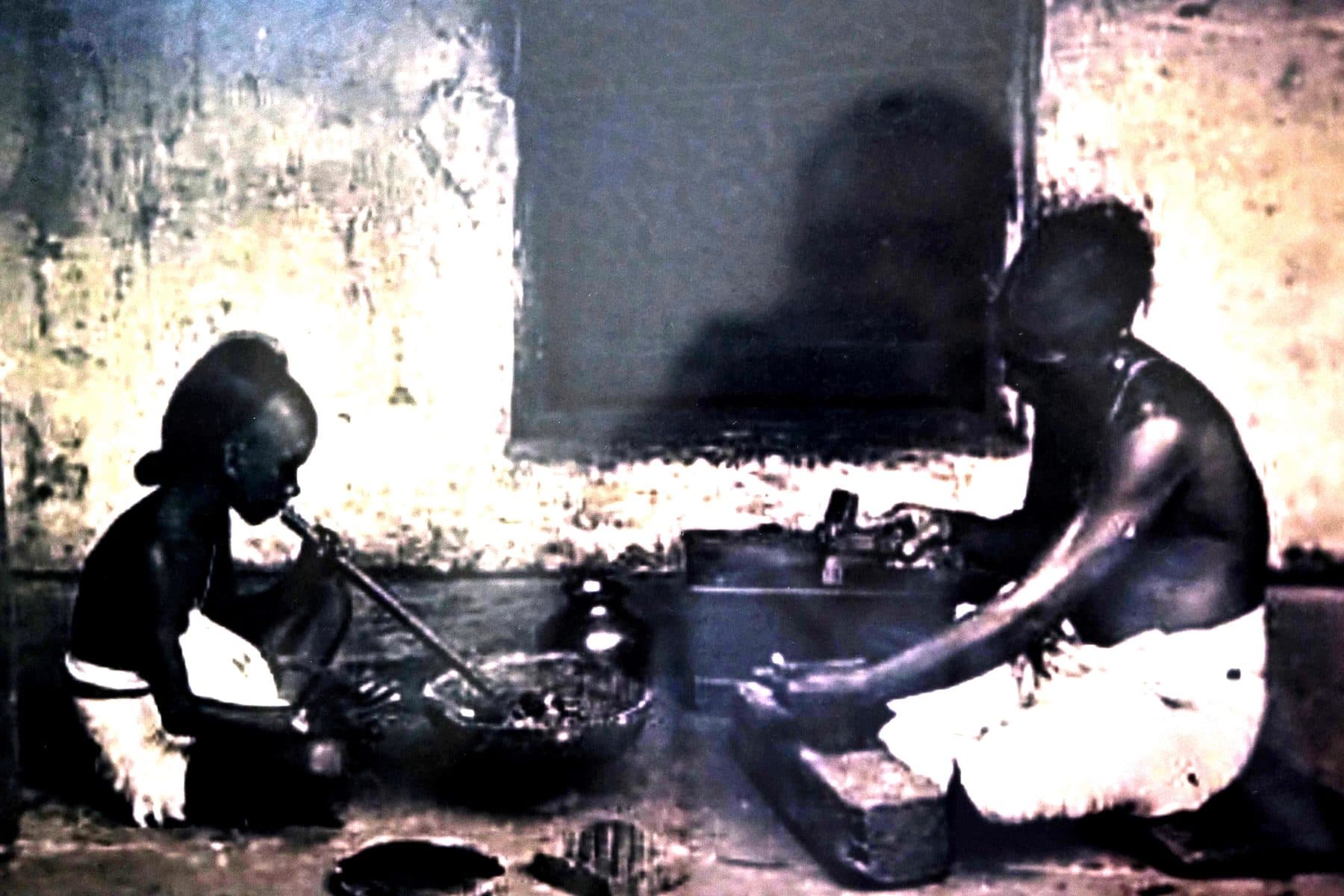 Archival photograph of a goldsmith and apprentice working a charcoal hearth with a blowpipe