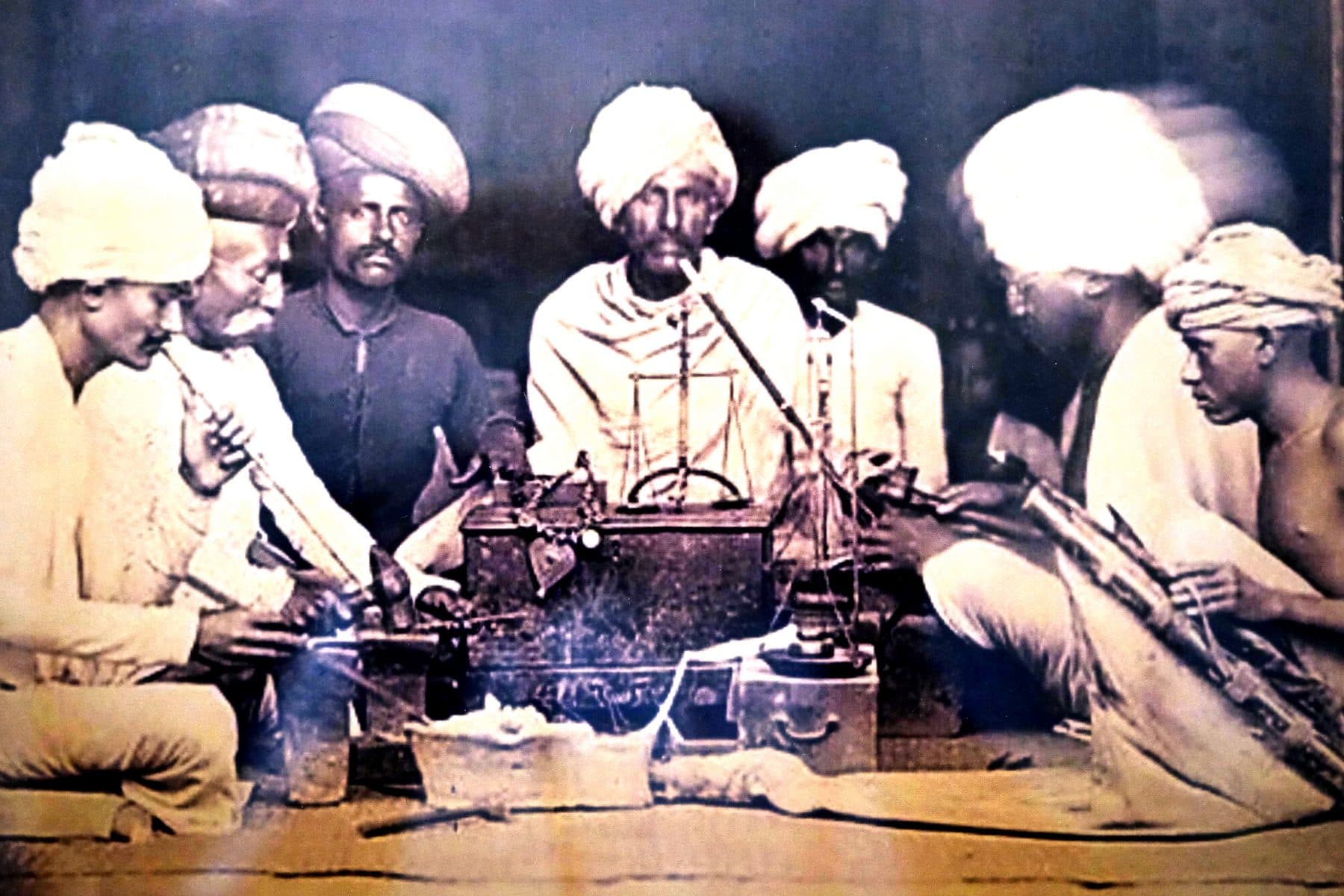 Archival group photograph of goldsmiths seated around a balance scale